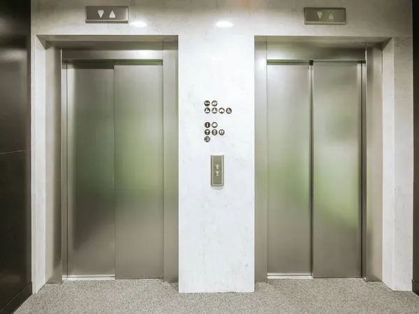 ホテル内の2つの新しいエレベーター。材料はステンレス鋼です。エレベーターの間に床の標識とエレベーターを呼び出すためのボタンがあります。 — ストック写真