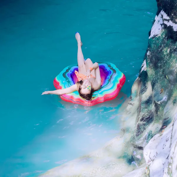 Ragazza sorridente che si copre gli occhi con lecca-lecca galleggia su un anello gonfiabile su un fiume turchese in una gola di canyon — Foto Stock