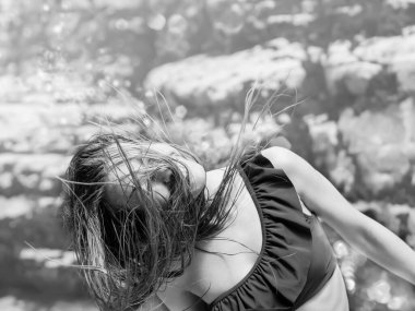 Bikinili bir kadın ıslak saçlarını bir kayanın arka planına doğru sallıyor. Yazın açık hava eğlencesi. Siyah beyaz fotoğraf