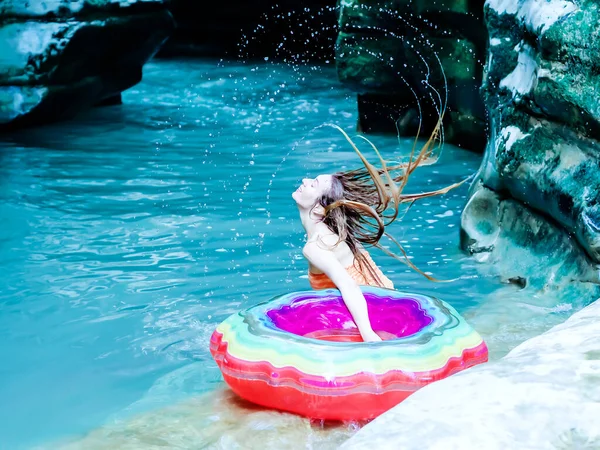 Ένα κορίτσι με ένα ουράνιο τόξο φουσκωτό δαχτυλίδι κουνώντας βρεγμένα μαλλιά της στο νερό του ποταμού σε ένα φαράγγι φαράγγι. — Φωτογραφία Αρχείου