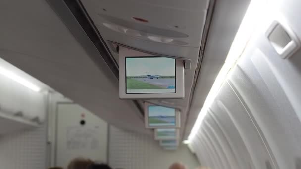 Russia, Adler 02.11.2021. A retractable monitor on the ceiling shows an advertisement for the aircraft. Board of the Utair aircraft. People in the cabin prepare for the flight. Selective focus — Stock Video