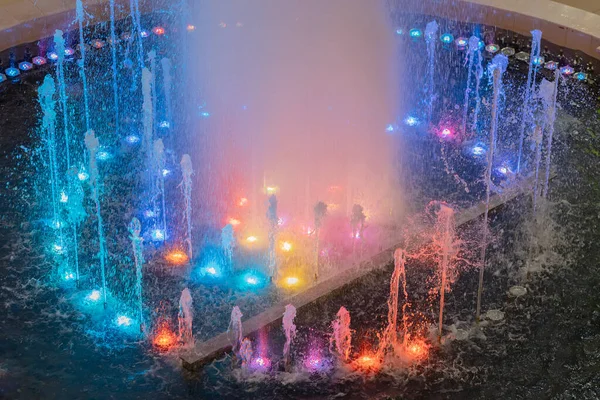 Μια πηγή με ρεύματα φωτίζεται από πολύχρωμα backlights. Πολύχρωμο σιντριβάνι. Μουσική πηγή — Φωτογραφία Αρχείου