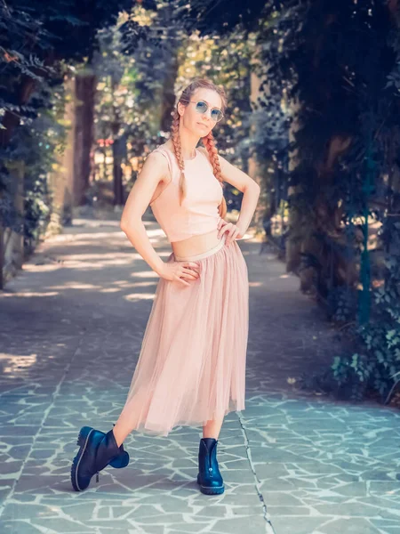 Женщина с косичками в пачке и грубой обувью позирует на аллее в летнем парке. — стоковое фото
