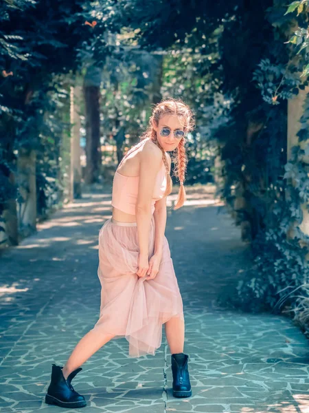 İki örgülü etekli ve sert çizmeli bir kız ayakları gölgeli yeşil bir parkta duruyor. Modern dansçı