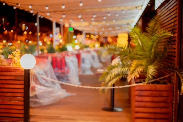 A blurry image of an idle street cafe, shielded by garlands and plastic-covered seats. Quarantine. Not a season. Blurred image — Stock Photo, Image