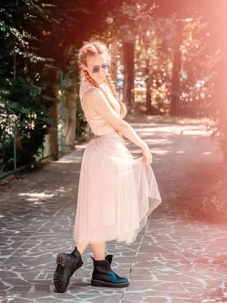 Una chica con dos coletas en un tutú y botas ásperas camina por un callejón en el parque. — Foto de Stock