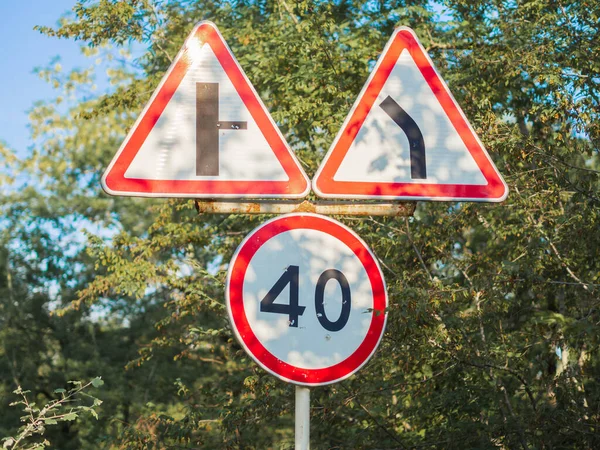 Triple road sign signifying speed limit and turning against green trees on a sunny day — Stockfoto