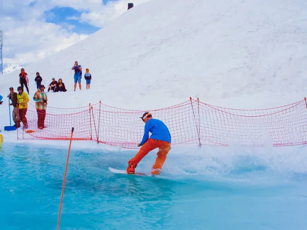 Rusia, Sochi 11.05.2019. Un tipo en una tabla de snowboard cruza un charco de agua sin caerse. Concurso de snowboard en el agua en la estación de esquí de Krasnaya Polyana. —  Fotos de Stock