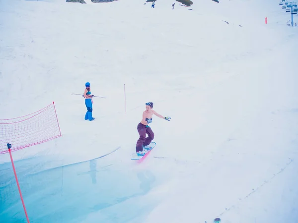 Ryssland, Sotji 11.05.2019. En tjej i byxor och baddräkt åker snowboard i en bassäng med vatten, medan andra idrottare tittar på henne. Tävlingar Krasnaya Polyana. — Stockfoto