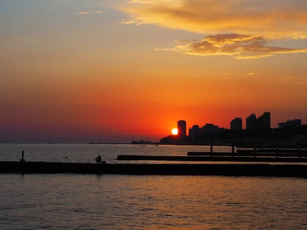 O sol põe-se no céu brilhante do por do sol acima das casas altas na beira-mar. Pôr do sol — Fotografia de Stock