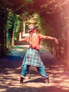 Şapkalı at kuyruklu kadın ve yeşil bir güney parkındaki gölgeli bir sokakta dans ederken giydiği büyük boy sokak kıyafeti. İşlem sonrası. Sanatsal etki