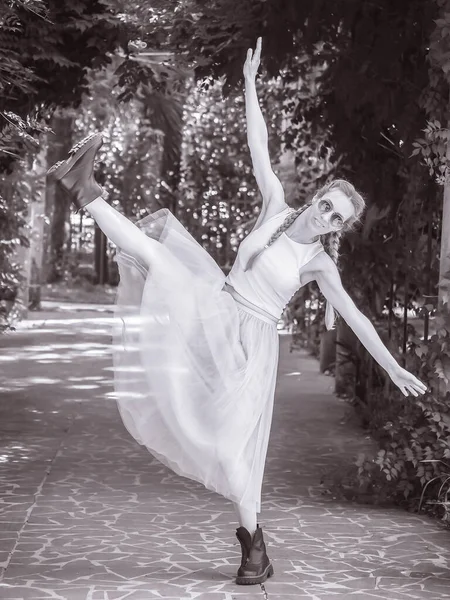 Balerin etekli ve sert çizmeli bir kız, kollarını parktaki bir ara sokakta sonuna kadar açıp sallıyor. Siyah beyaz fotoğraf