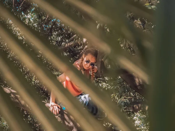 View through the palm branch of a girl sitting on a tree. Blur focus — Fotografia de Stock