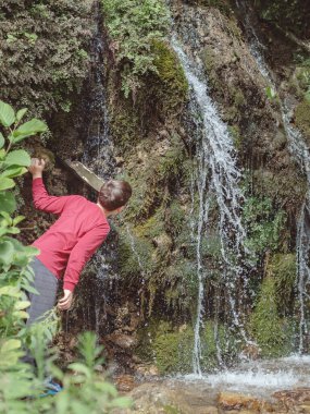 Bir çocuk, yosunla kaplanmış bir kayadan akan pınardan su içer..