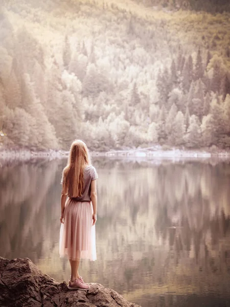 Eine Frau blickt in die Ferne, die am Rande eines Steins in der Nähe eines klaren Waldsees steht. Naturschutzgebiet. Weicher Fokus lizenzfreie Stockfotos