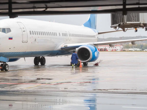 Een man in een blauwe regenjas nadert de motor van een vliegtuig op de baan op een regenachtige dag. Onderhoud van luchtvaartuigen — Stockfoto