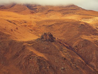 Bulutlar, ortasında yüksek kayalık bir tepenin bulunduğu kızıl sonbahar dağ vadisine indi.