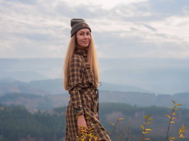 Gülümseyen uzun saçlı bir bayan bulutlu bir gökyüzünün altında ağaçlık tepelerin arka planında duruyor. Kafkasların güzelliği. Kislovodsk Parkı
