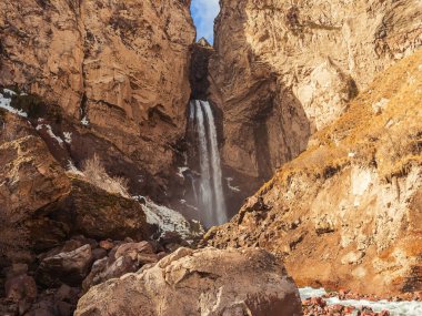 Yüksek bir dağ şelalesi, güneşli bir sonbahar gününde Kuzey Kafkasya 'daki banliyö vadisinin kayalıklarından aşağı akar.