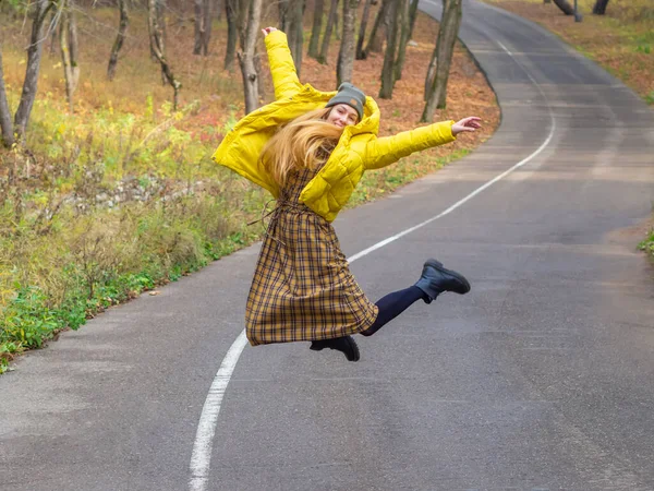 Γελώντας γυναίκα στη σύγχρονη στολή πηδώντας πάνω από την εκκαθάριση στενό δρόμο στο πάρκο φθινόπωρο — Φωτογραφία Αρχείου