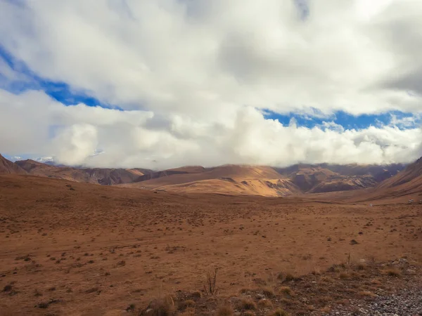 Höstfältet ligger i de kaukasiska högländerna med vita moln som stiger ner på bergstopparna och en blå himmel som kikar genom dem — Stockfoto