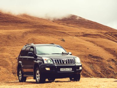 Rusya, Kislovodsk 02.11.2021. Güzel, siyah, yeni bir araba, dağların arasında bir sonbahar çayırında duruyor. Tepelere sis çöküyor..