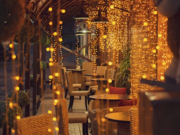 Un acogedor café vacío en la iluminación de la noche de muchas guirnaldas ubicadas en la terraza. Enfoque suave Fotos De Stock