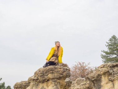 Parlak sarı ceketli bir bayan bulutlu bir gökyüzüne karşı bir tatil köyü parkında uçurumun kenarında oturuyor. Sonbaharda Kislovodsk 'ta dinlen.