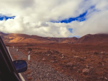 Kafkaslar 'ın dağ vadisindeki sarı sonbahar tarlalarında dağ zirvelerine beyaz bulutlar iniyor. Fotoğraf hareket halindeki bir arabanın camından.