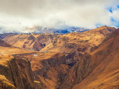 Elbrus yanardağının etkin olmayan bölgesinde, dağ vadisinin sonbaharının ihtişamı kalın beyaz bulutların arkasında gizlidir.