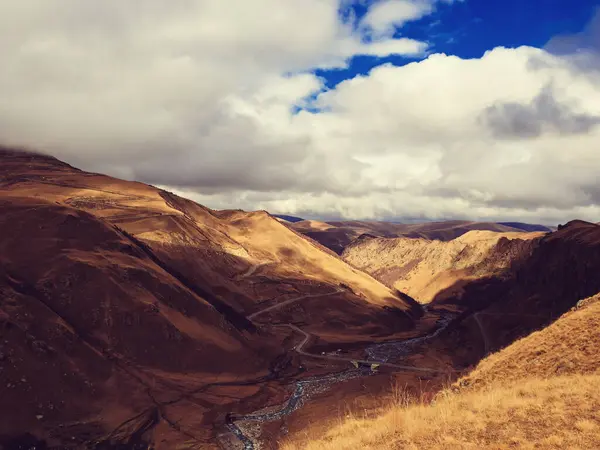 A serpentine river flows in the gorge of a mountainous autumn valley. Serpentine road and bridge over the river in the high Caucasian mountains