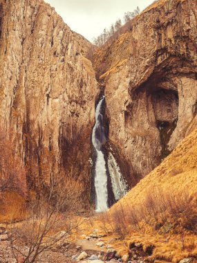 Aralarından güçlü bir şelale akan yüksek dik sonbahar kayaları. Jily-su Şelalesi
