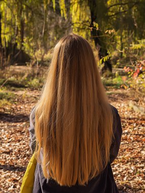Uzun dalgalı saçlı sarışın bir kadın sonbahar parkında güneşli bir günde ayakta duruyor. Arkadan bak. Doğallık kavramı