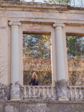 Bir kadın, güneşli bir sonbahar gününde büyük pencereleri ve sütunları olan terk edilmiş ve aşırı gelişmiş bir Yunan tarzı binanın kalıntılarında yürüyor.