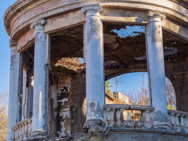 Yunan tarzında sütunları ve sütunları olan, ağaçlarla kaplı ve çatısının kırık olduğu terk edilmiş bir restoranın yarı dairesel parçası.