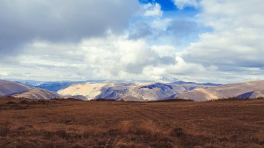 Kahverengi sonbahar tarlası Kafkasya dağlarında bir dağ vadisine bakan ve mavi gökyüzünde yemyeşil bulutlar