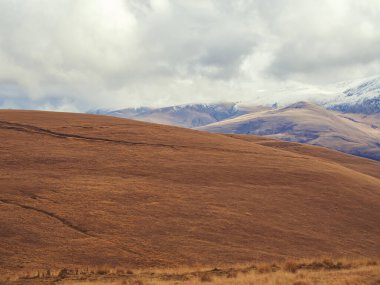 Kuru çimlerle kaplı kahverengi sonbahar dağları ve sarkık bulutlarla kaplı tepeler.