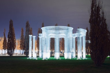 Yuvarlak, aydınlık bir çerçeve sütunu bulutlu bir gökyüzünün altındaki yeşil bir çimenliğe kurulur.
