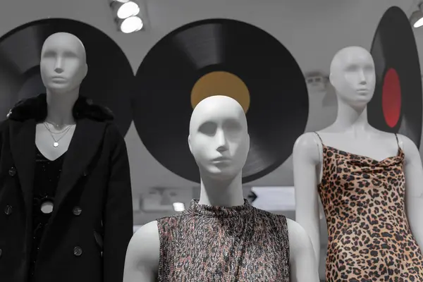 A white female mannequin in a clothing store next to other mannequins against a backdrop of vinyl record decor. Selective focus.