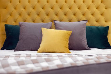 Çok renkli yastıklar, yumuşak sarı kadife bir yatak başlığı ve kareli yatak örtüsü olan bir yatakta yatıyor. Orta odaklı tam ekran fotoğraf