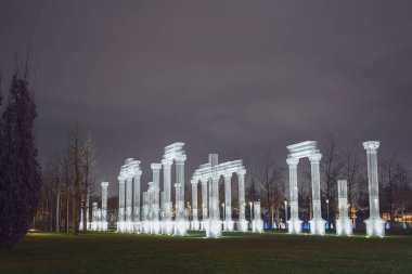 Rusya, Krasnodar 07.01.2022. Spot ışıklarıyla aydınlatılan dekoratif çerçeveli beyaz sütun bulutlu bir gökyüzünün altındaki kış gecesi parkına monte edilir.