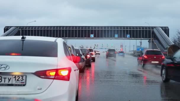 Ryssland, Krasnodar 04.01.2022. En linje av bilar på en bred motorväg i regnigt väder. Fyra körfält. Väntar på grönt ljus. Rörelse i din egen fil. — Stockvideo