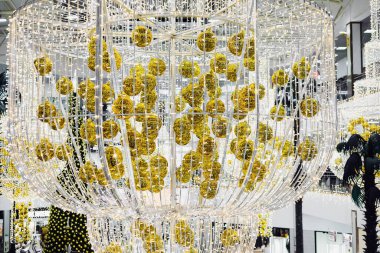 Altın Noel topları ve bir çelenkle süslenmiş büyük bir avize bir alışveriş merkezinde asılı duruyor.