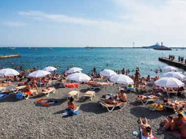 Deniz plajı şemsiyelerin altında güneşlenen insanlarla dolu. Yaz tatili.