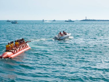Bir grup insan yaz günü denizde bir tekneye bağlanmış şişme bir muza biniyor. Güneyli aşırı eğlence