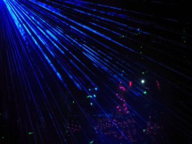 Karanlıkta parlayan çok renkli ışıkların arka planına karşı parlak mavi neon ışınları. Lazer gösterisi. Bulanık resim