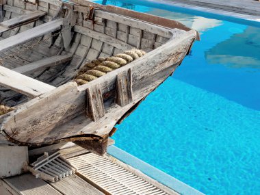 Mavi şeffaf açık havuzun kenarında eski bir ahşap tekne duruyor. Klasik denizcilik dış dekorasyonu.