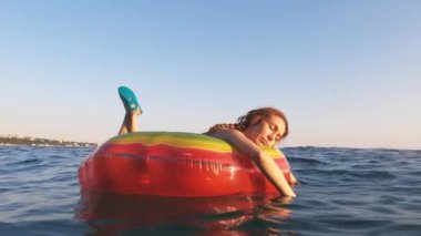 Bir kadın deniz dalgalarında sallanan şişme, parlak bir şamandırada yüzüyor. Deniz gevşemesi. Yaz tatili. 4K