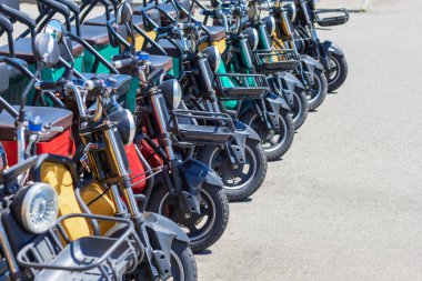 Güneşli bir günde farları ve sepetleri olan çok renkli elektrikli bisikletler sıralanır. Turistler için yürüyen kiralık.