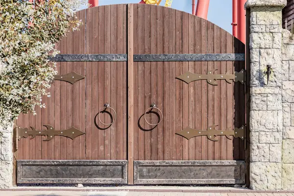 Rounded wooden gate with round door handles and medieval style metal decor in an amusement park on sunny day